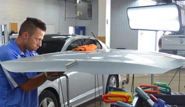 Paintless dent removal technician Alexandre Chabert repairing the hood of a car.